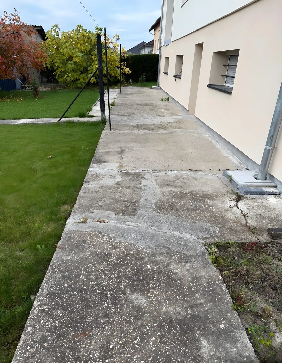 Ancienne allée en béton fissurée et dégradée le long d'une maison, avant travaux