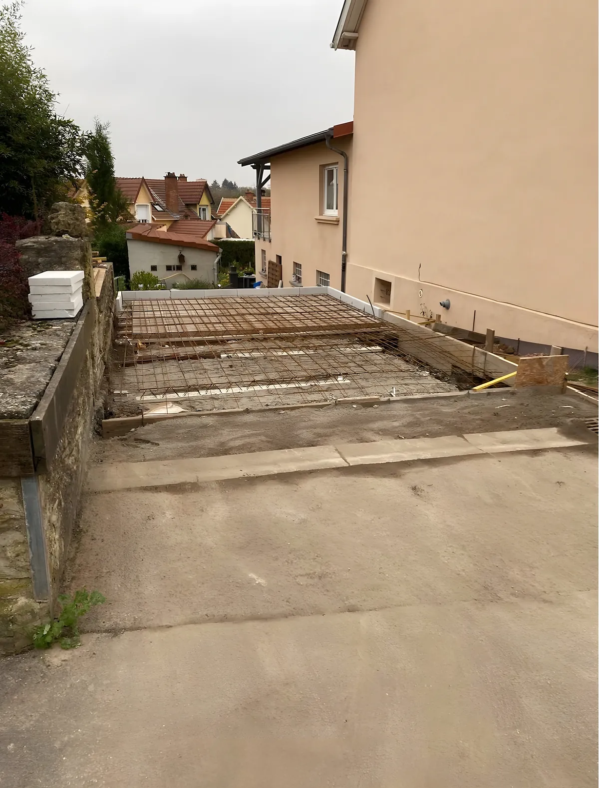 Ferraillage en treillis soudé et coffrage en place avant le coulage d'une dalle béton contre une maison