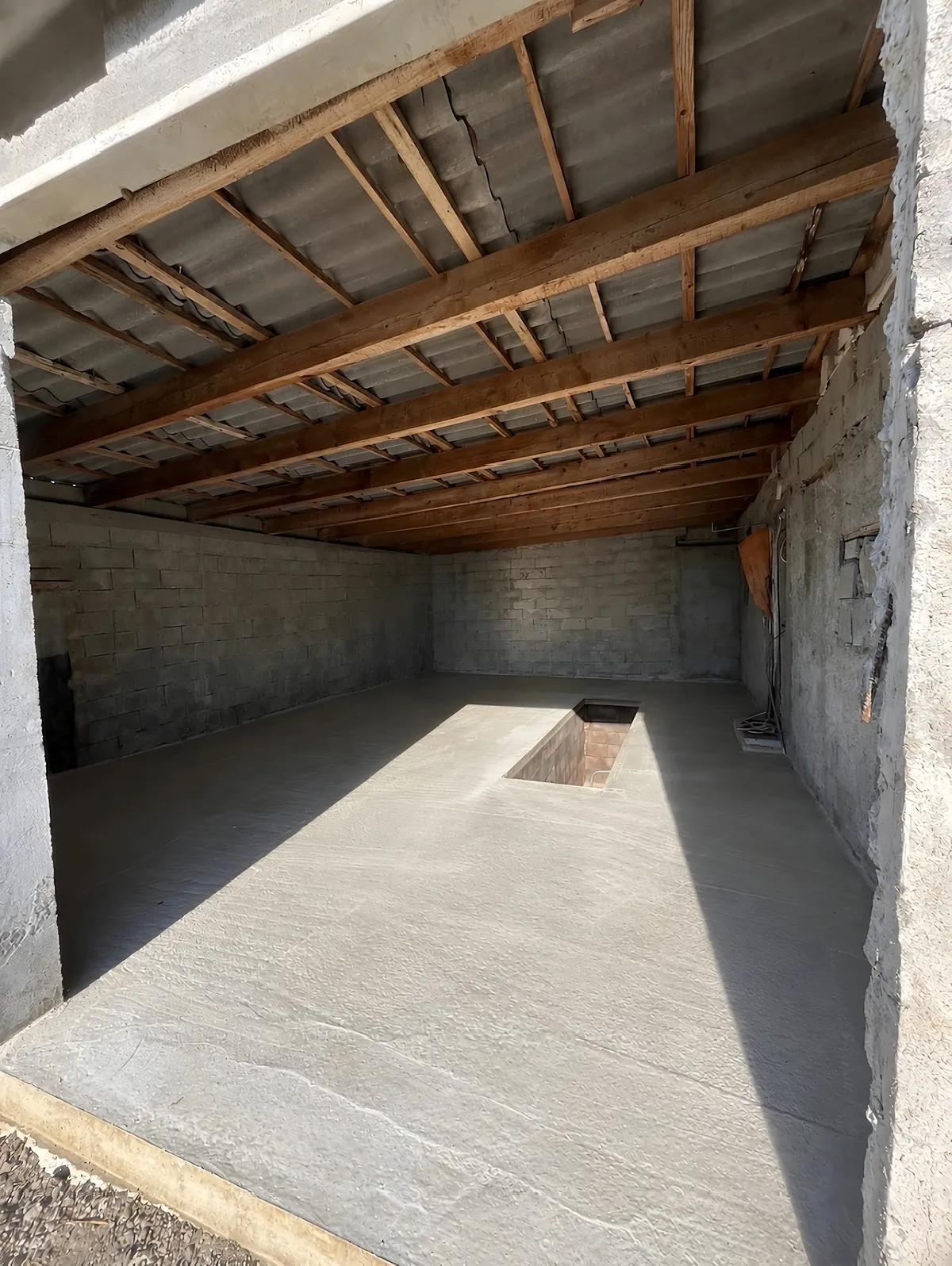 Garage après travaux avec une dalle béton neuve et une fosse maçonnée au centre