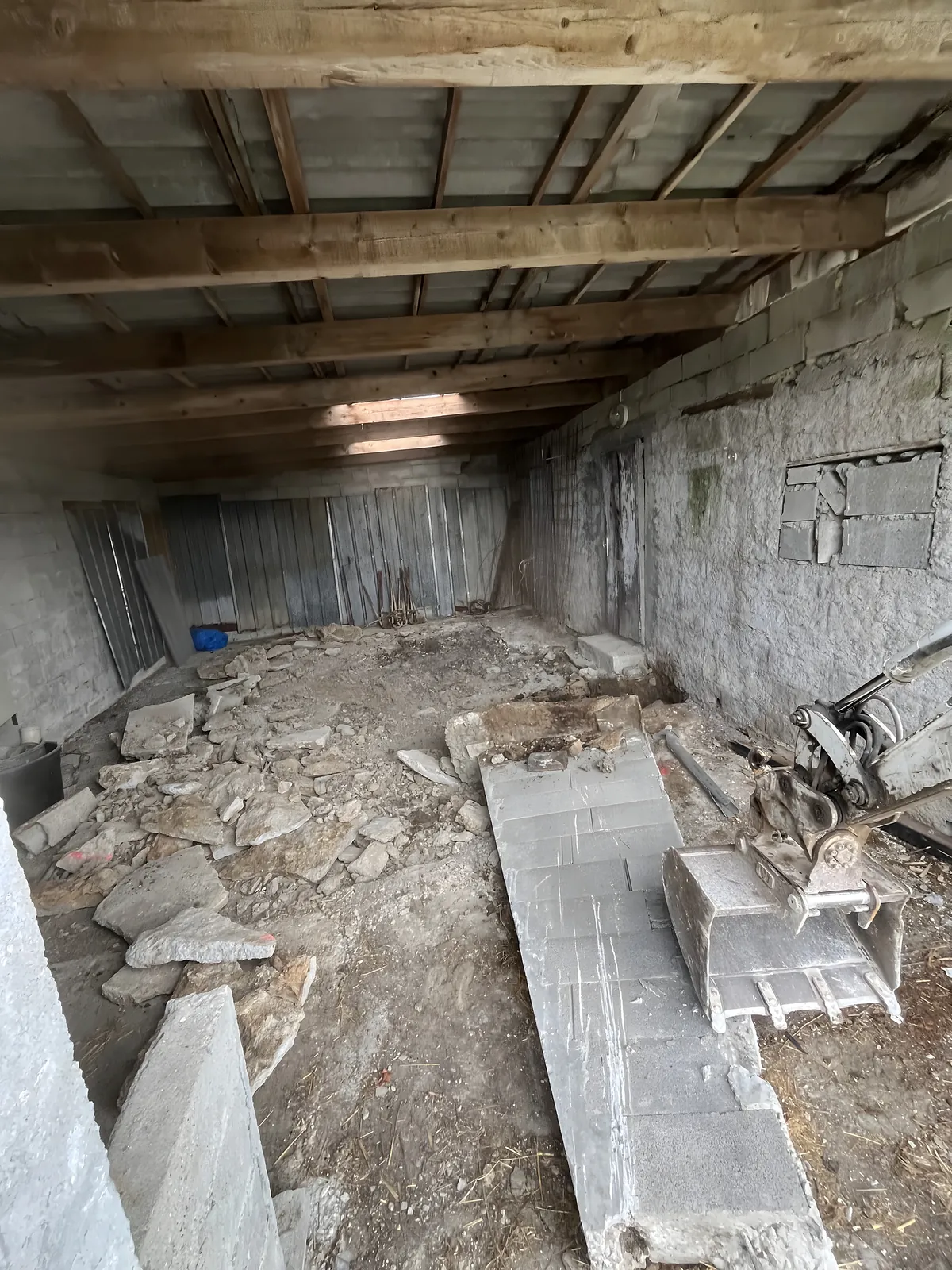 Intérieur d'un ancien garage avant travaux, sol démoli et gravats, mini-pelle à l'entrée