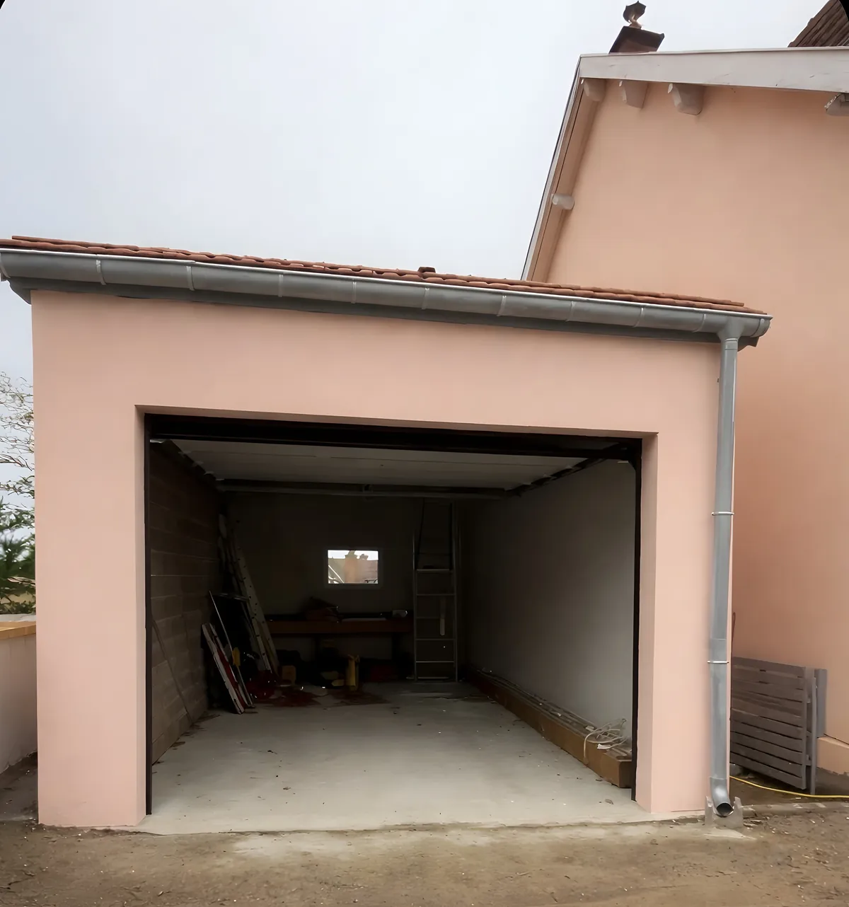 Garage maçonné enduit, accolé à une maison, porte ouverte sur un intérieur en blocs béton