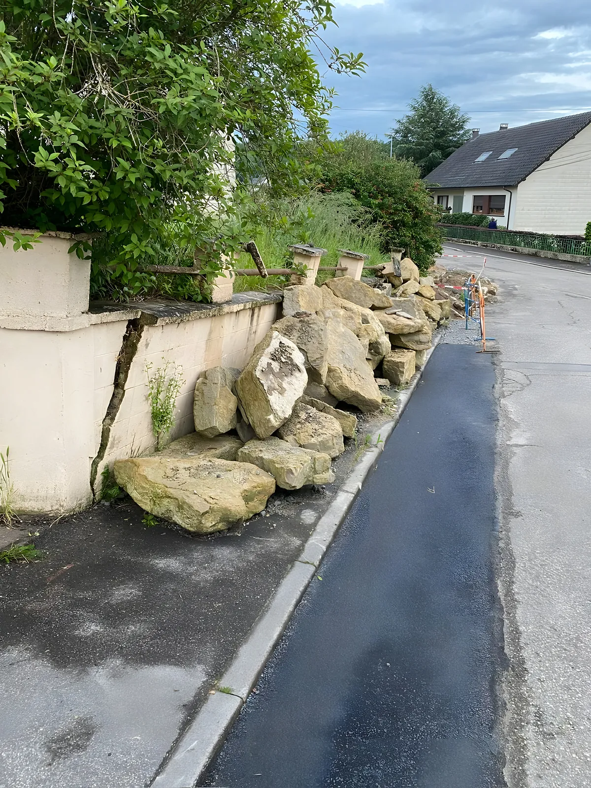 Mur de clôture fissuré et blocs de pierre effondrés le long d'un trottoir, avant intervention