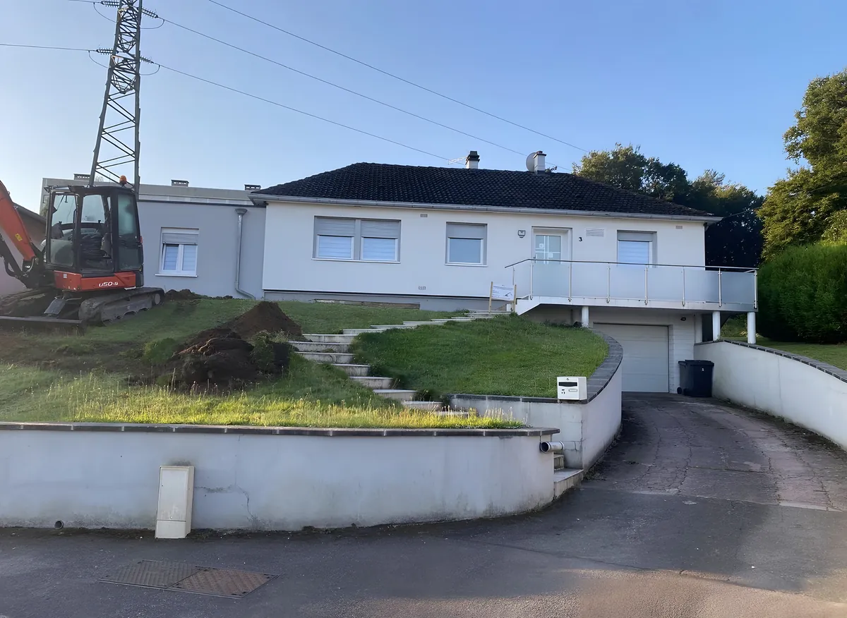 Terrain en pente engazonné devant une maison avant la création des murs de soutènement